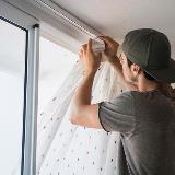 Person installing curtains inside a home with an open window