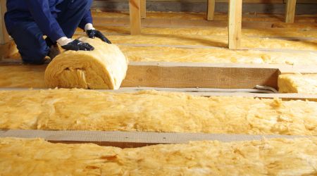 A person wears gloves and unrolls insulation in an attic