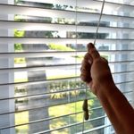 hand pulling cord of mini-blinds on window