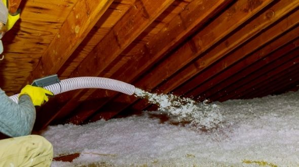 person blows in insulation into attic