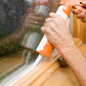 A person applies silicone caulk to seal a window frame