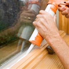 A person applies silicone caulk to seal a window frame