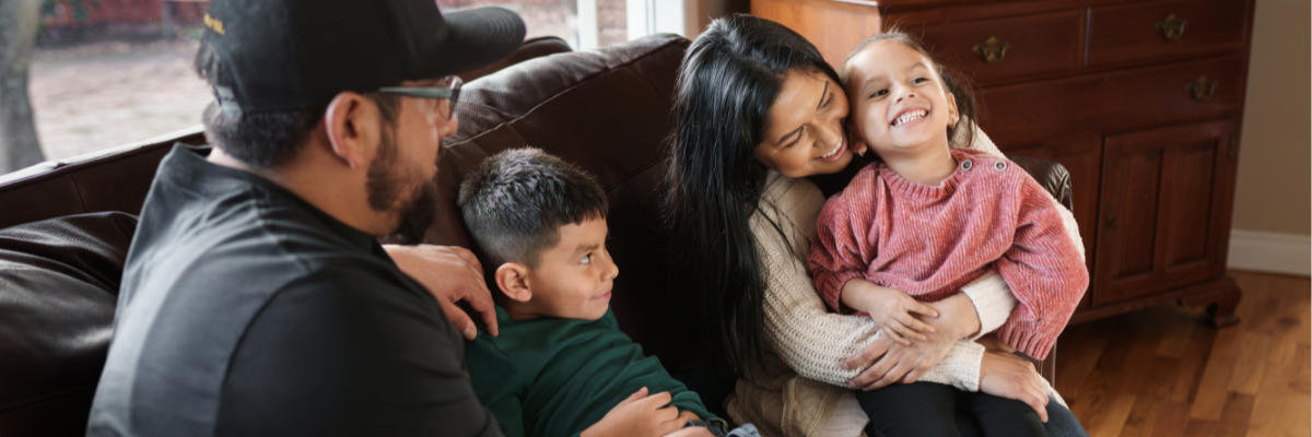 a mom and dad sit on a couch with their two young children