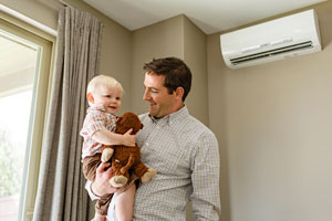 a father holds his baby with a ductless heat pump in the background