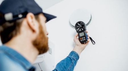 a man wearing a baseball hat uses a heat reading sensor on an energy audit