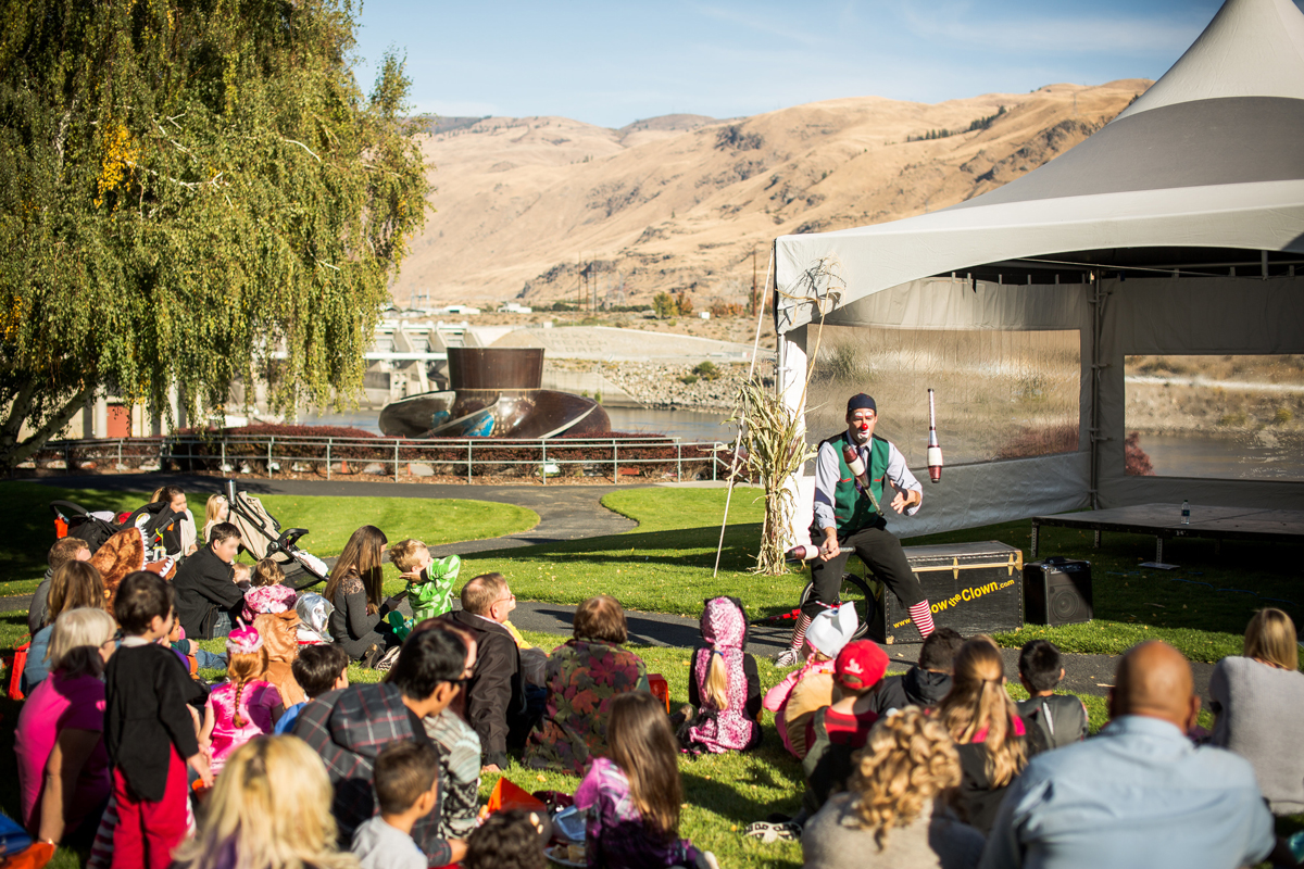 Photo of L-Bow the clown juggling in front of a crowd, with Rocky Reach Dam in the background 