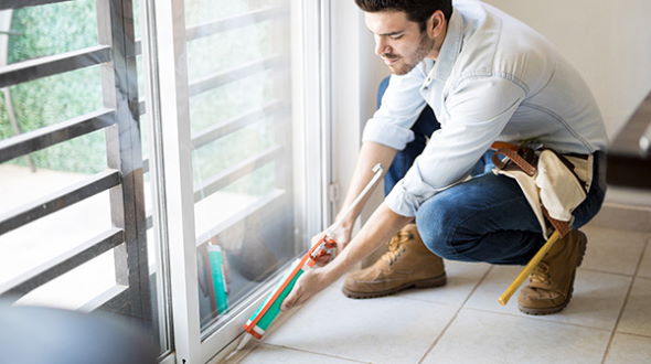 Person uses caulking gun to seal around sliding glass door