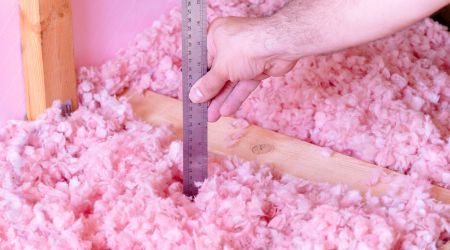 a hand holding a ruler into loose insulation