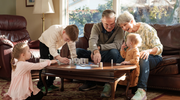 Grandparents sit on a couch with their grandchildren and play dominos