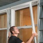 man installing storm window on the outside of a house window