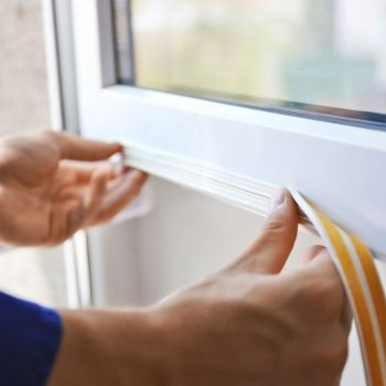 a person applies weather stripping to seal a gap in a window