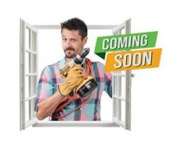 A man stands in an open window holding a drill